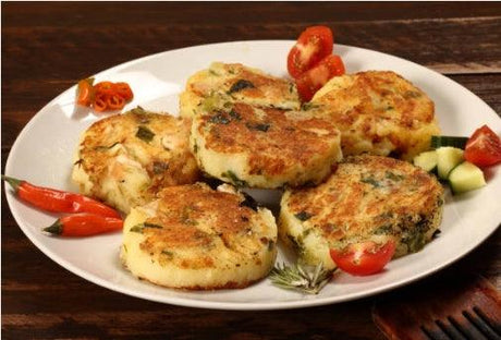 A plate of golden-brown potato cakes garnished with cherry tomatoes, red chili peppers, and herbs