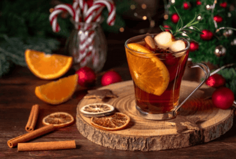 A glass of mulled wine with orange slices and cinnamon sticks, set on a wooden table with festive decorations.