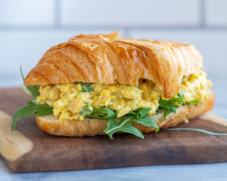 Curried egg sandwich with arugula served on a flaky croissant, placed on a wooden cutting board