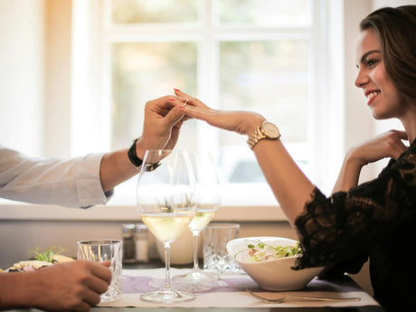 Man proposing to woman at a romantic dinner table with wine glasses and a ring