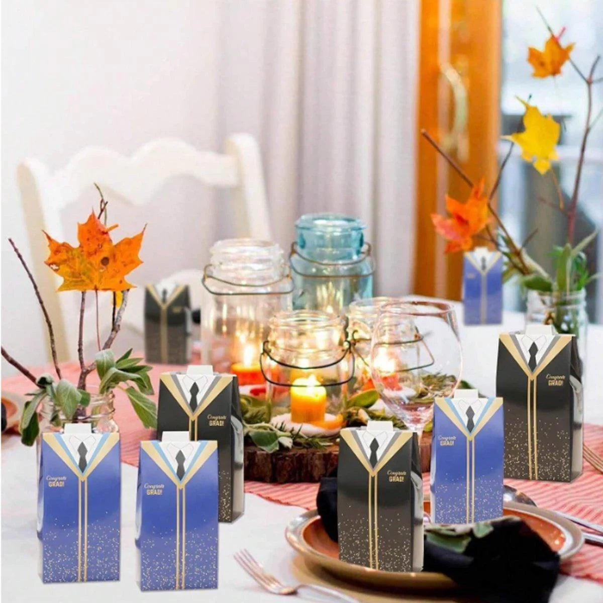 A festive party table with fall decorations and graduation gown-shaped candy boxes.