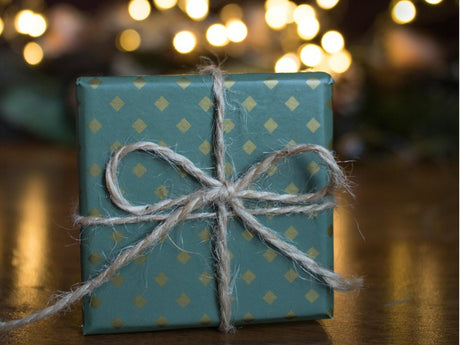 A gift wrapped in teal paper with gold dots is tied with a rustic twine bow