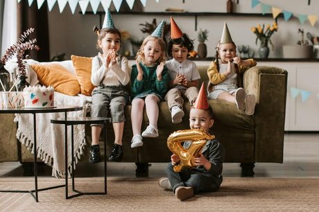 A group of children wearing party hats sits on a couch, celebrating a birthday