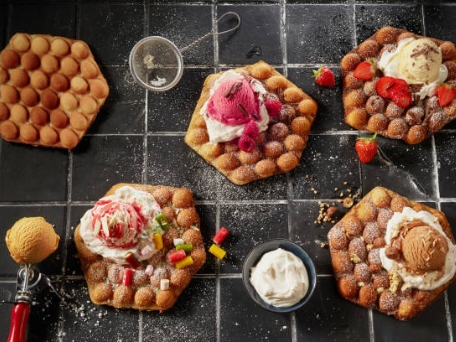 Various bubble waffles are topped with ice cream, strawberries, whipped cream, and colorful candies