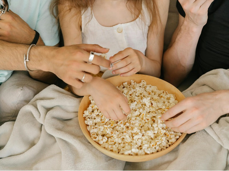 A group of people is sharing a large wooden bowl of popcorn, enjoying a cozy moment together