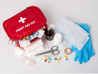 A red first aid kit with a white cross is open, revealing various medical supplies including bandages, scissors, gloves, and medication