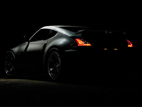 A sleek, dark-colored sports car is shown in a low-light setting with its taillights illuminated