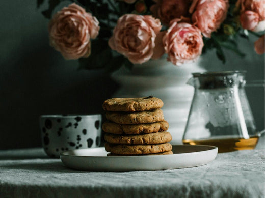 a stack of cookies on a plate, with a cup and a glass pitcher nearby