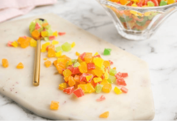 A marble cutting board with colorful diced crystal candies and a gold spoon