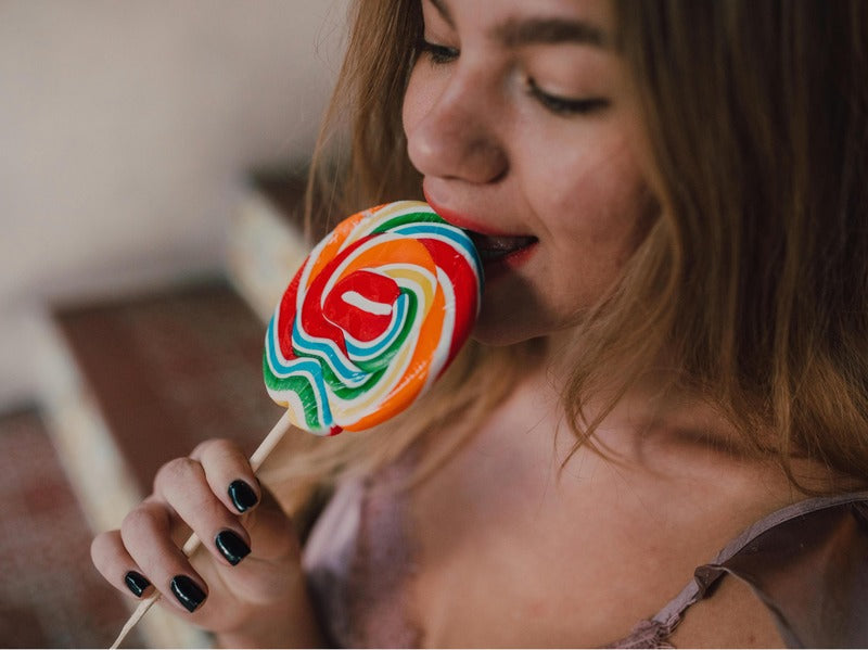 A woman with black nail polish is enjoying a colorful swirl lollipop