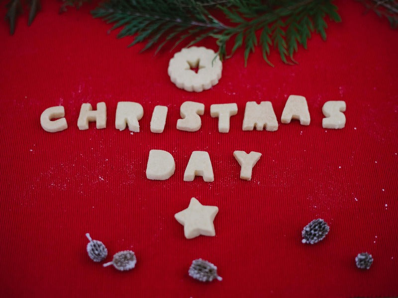 Letter-shaped cookies spell out "CHRISTMAS DAY" on a red background with festive decorations