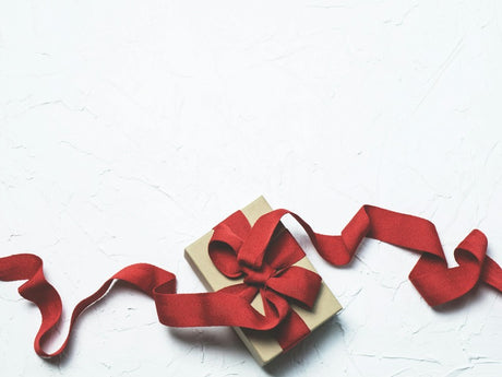 A gift box wrapped in brown paper is adorned with a red ribbon that forms a bow and trails