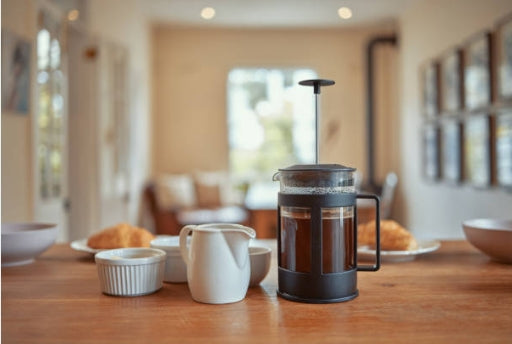 A French press coffee maker sits on a wooden table