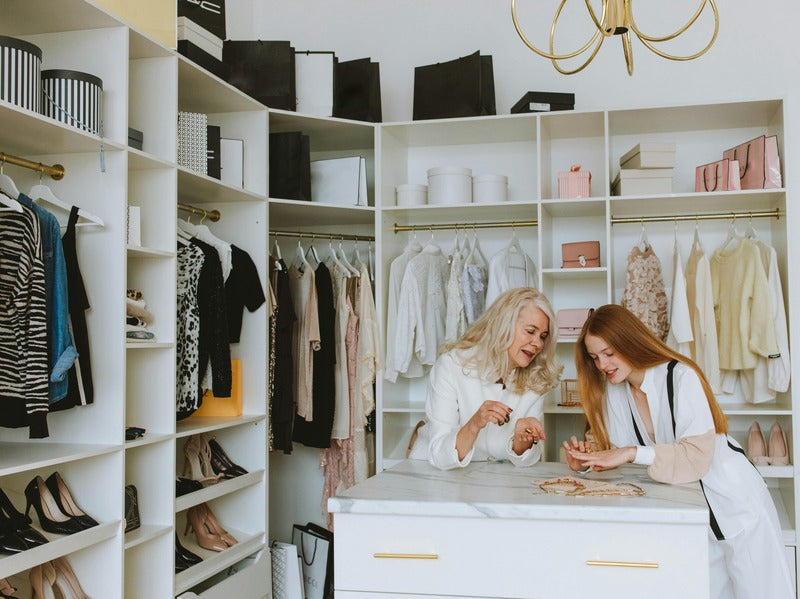 Two women are happily engaged in a conversation while sorting through jewelry in a well-organized, stylish closet