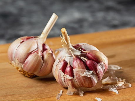 two garlic bulbs with purple skin, partially peeled and placed on a wooden surface