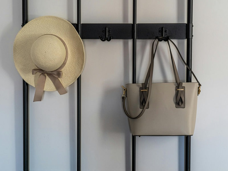 a beige handbag and a straw hat hanging on a black wall hook, creating a simple and organized display