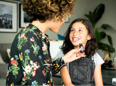 a woman and a young girl smiling at each other, with the woman holding a bottle of essential oil near the girl's face