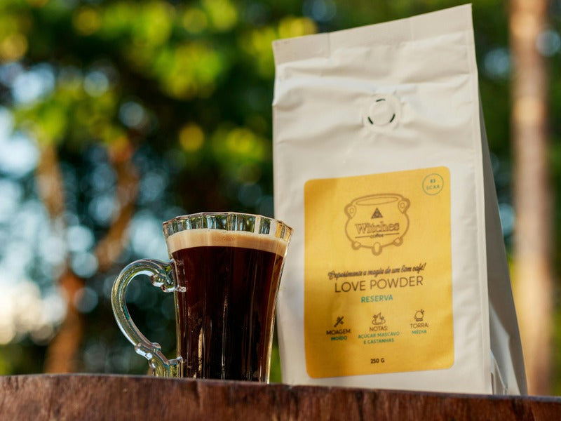 A cup of coffee sits next to a coffee bag labeled "LOVE POWDER RESERVA" on an outdoor table