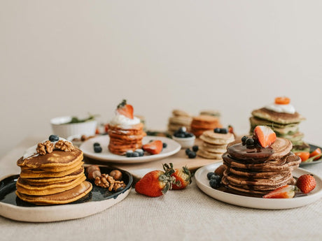 Assorted stacks of pancakes with different toppings, including chocolate, nuts, berries, and whipped cream