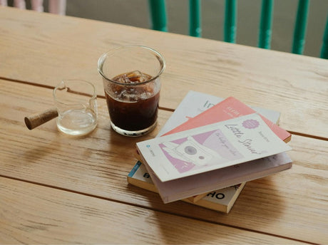 Iced coffee served in a glass alongside books and a small glass pitcher