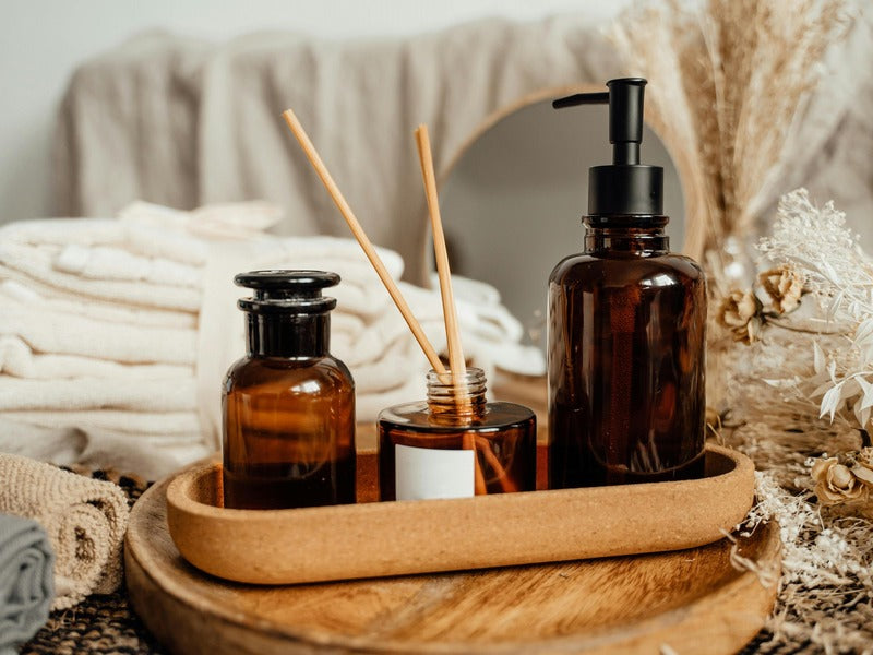 a beautifully arranged set of amber glass bottles, including a reed diffuser and a pump dispenser