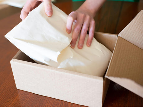Person unpacking a product from a cardboard box with protective paper