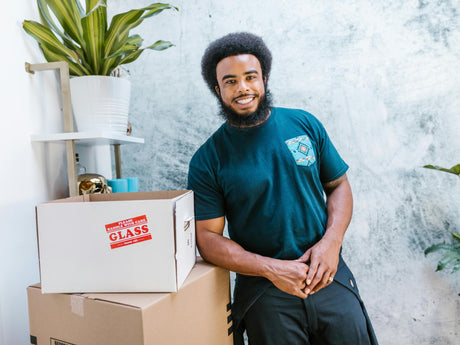 Smiling mover standing beside labeled fragile cardboard boxes during a home relocation